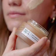 Close-up of a smear of UpCircle Night Cream on a woman's cheek as she holds the open jar beneath her chin.