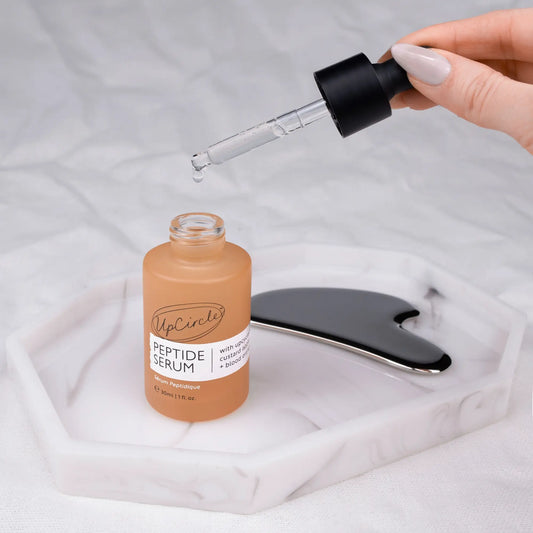 UpCircle Peptide Serum bottle with dropper and gua sha tool on a white background