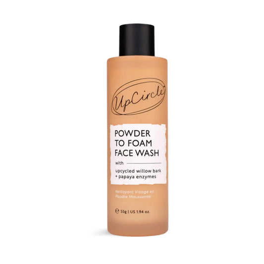A bottle of UpCircle Powder to Foam Face Wash, featuring a warm peach-beige translucent bottle, a black cap, and a white label with black text.