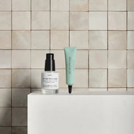 Bottle of On The Wild Side anti-blemish serum next to a Spot Solution treatment tube in a bathroom setting.