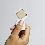 Close-up of a hand holding open Uoga Uoga Luminous cream highlighter compact showing shimmery texture