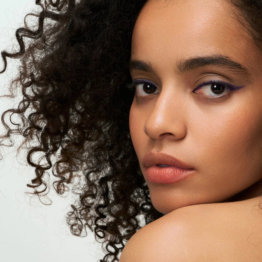Close-up of person with curly hair wearing Eclo eyeliner pencil Prune Velours on light background